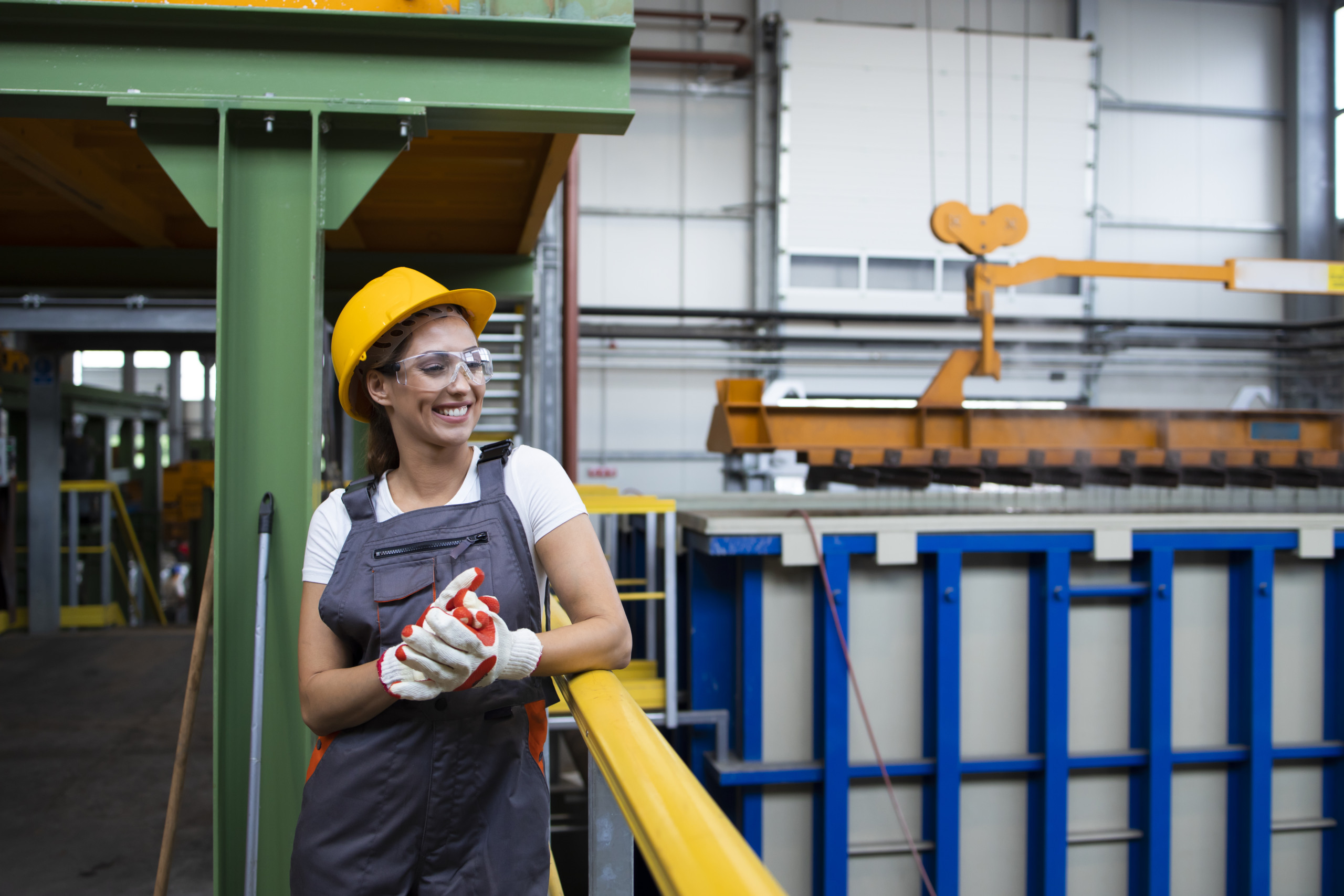 Portrait of smiling female factory worker standing in industrial production hall.