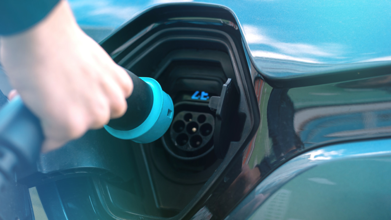 Man plugging in charger into an electric car at charge station Man plugging in charger into an electric car at charge station