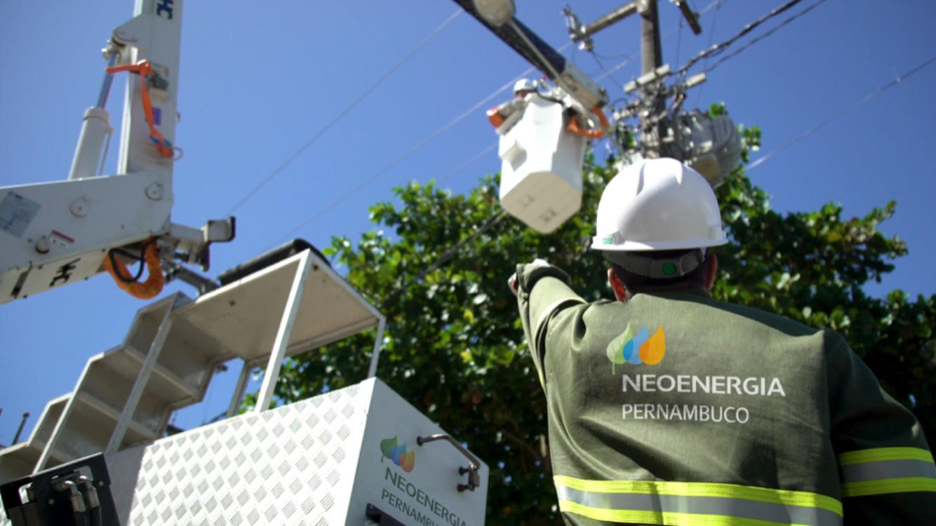 Eletricista com camisa da Neoenergia Pernambuco próximo a poste da rede de distribuição